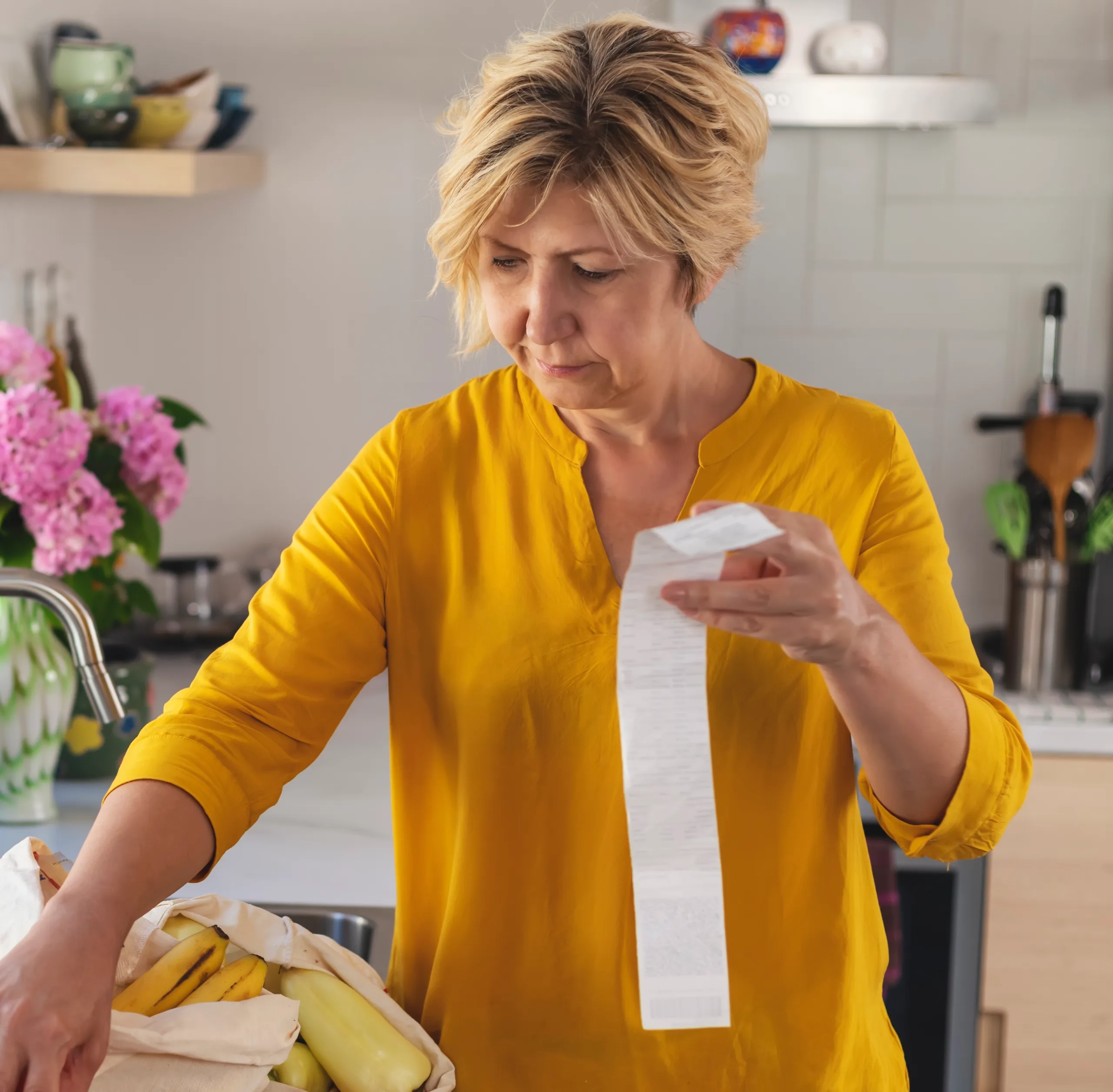 Shopper at home reviewing a grocery receipt at the kitchen sink.