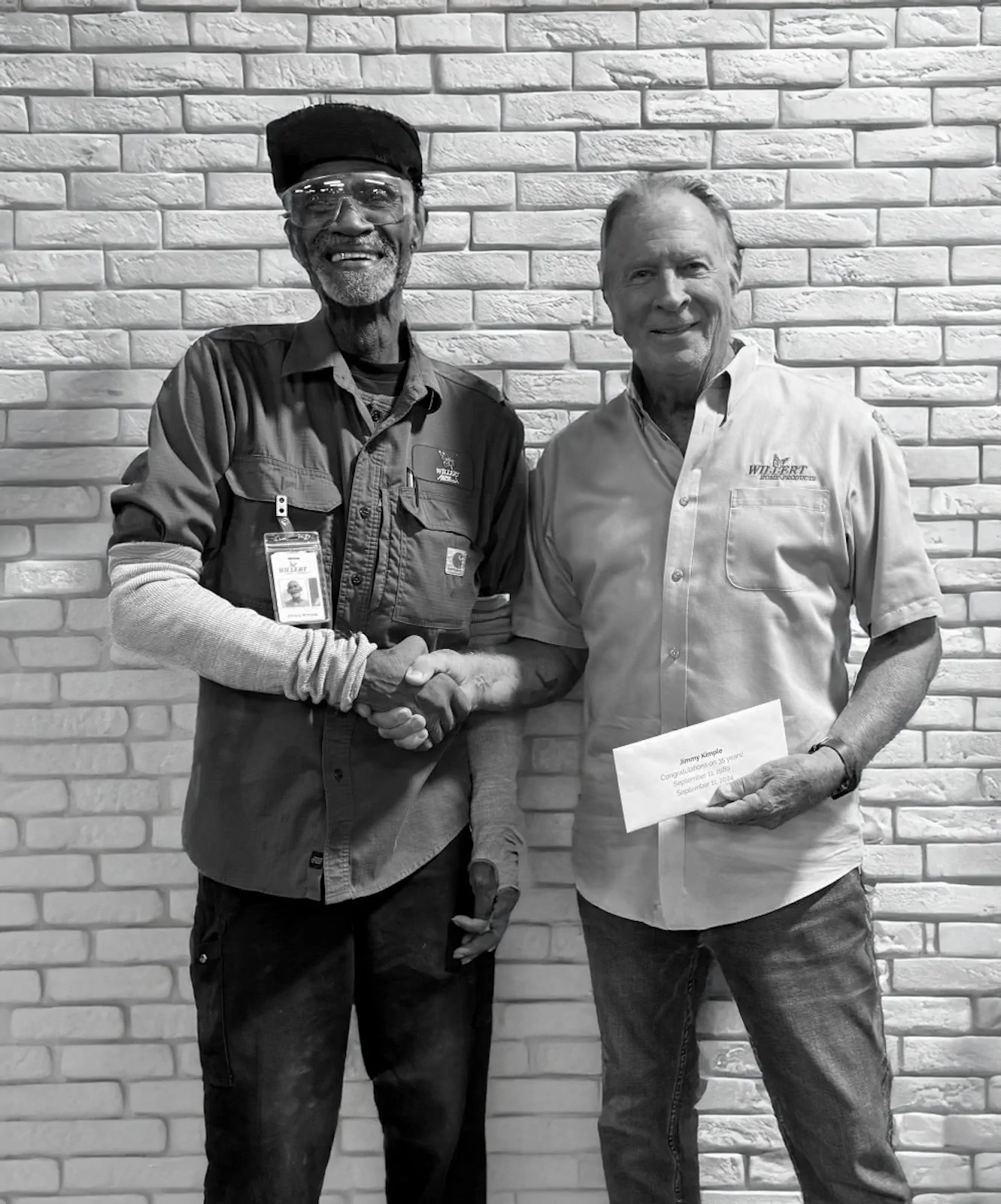 Two members of the Willert team shaking hands in front of a brick wall — black and white portrait.